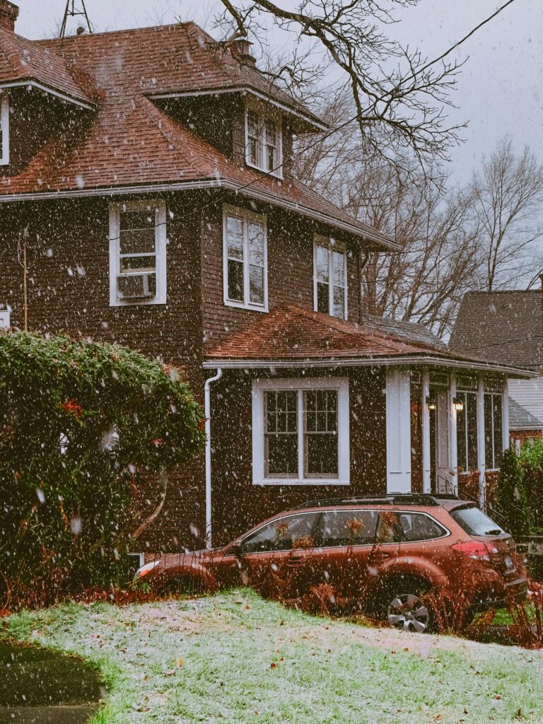 A picturesque vintage house surrounded by snow with a classic car parked outside.