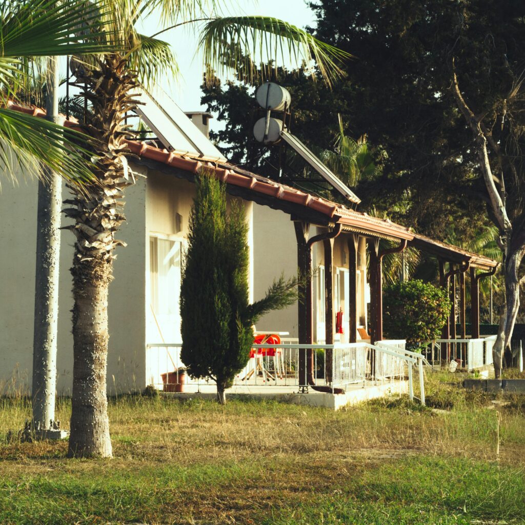 A warm view of a quaint bungalow surrounded by lush palm trees and greenery under a clear sunny sky.