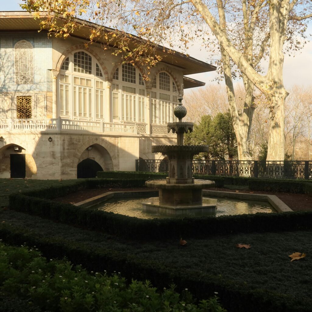 Serene garden view with a historical mansion and fountain under autumn skies.