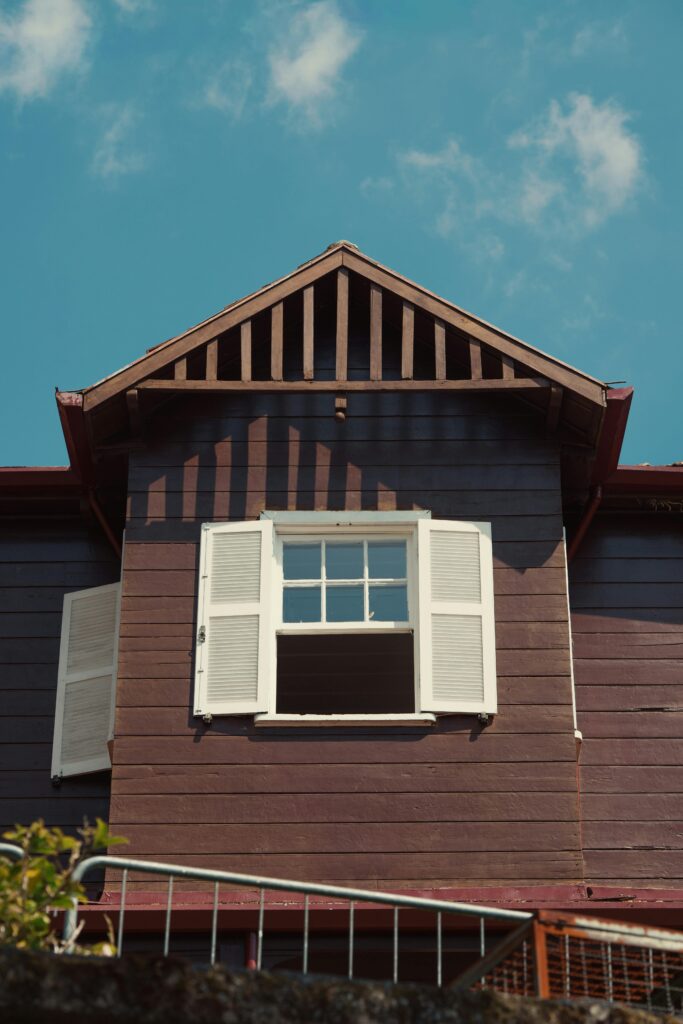 A rustic wooden house with open shutters against a clear blue sky, exuding warmth and charm.