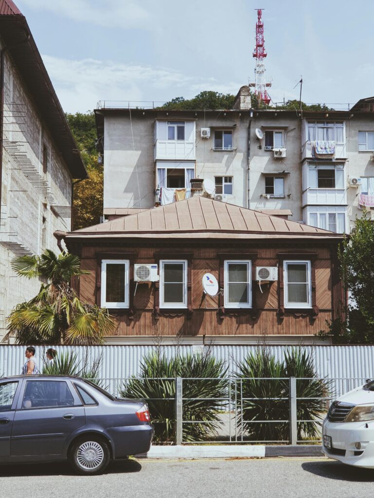 Street view with cars parked by a wooden house, featuring urban and residential architecture.